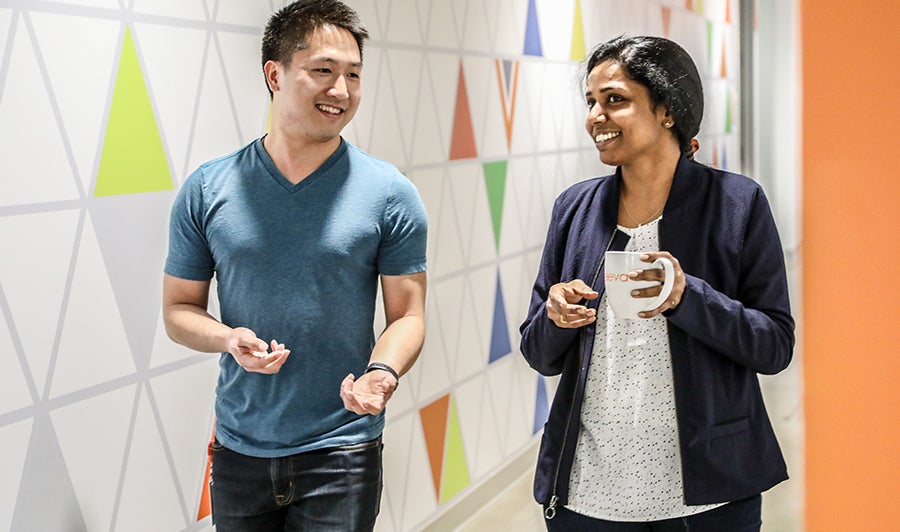 Smiling male and female Veeva colleagues walk and talk down a vibrantly painted hallway